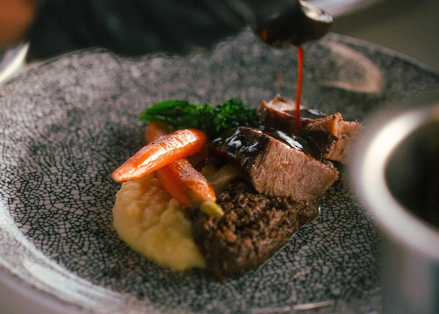 Sauce poured over a plated steak and vegetables during a FlyDining dinner